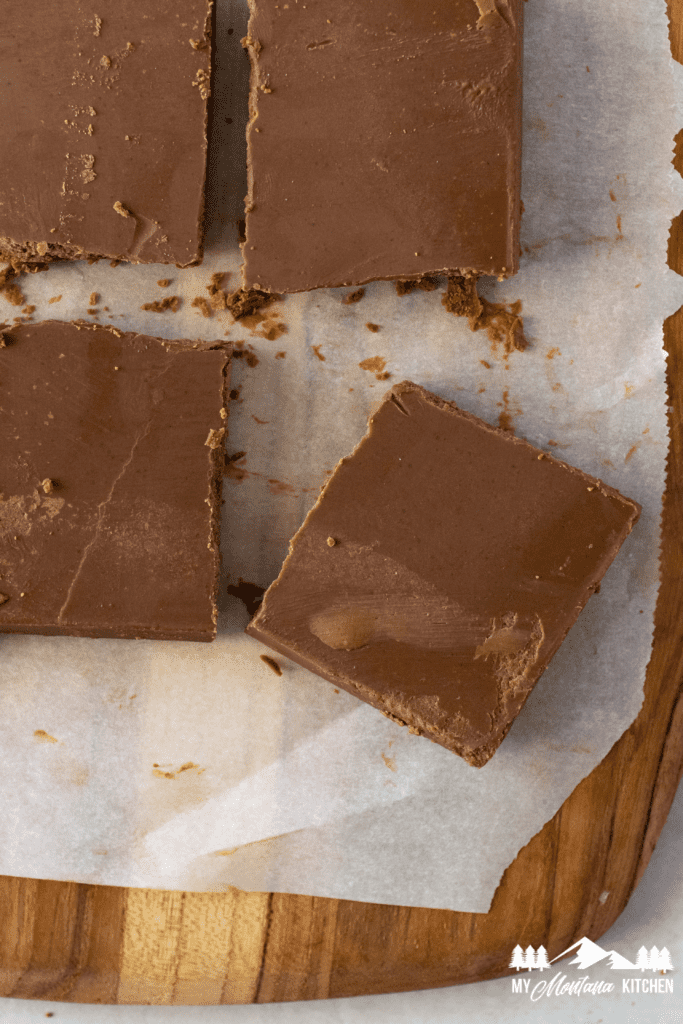 chocolate peanut butter fudge cut into squares on wooden cutting board with parchment paper