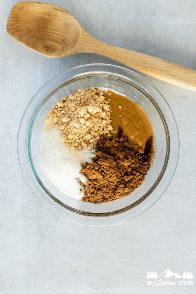 ingredients for peanut butter chocolate fudge in a glass bowl with wooden spoon