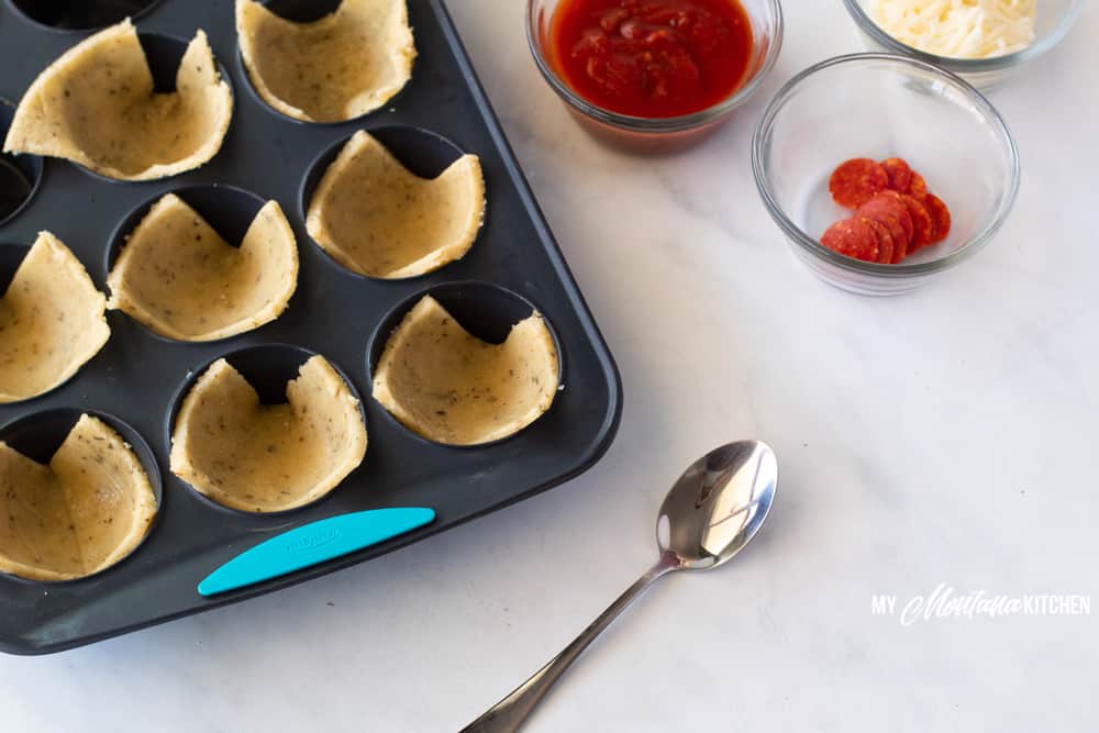 trim healthy mama pizza dough in muffin tin with pizza sauce