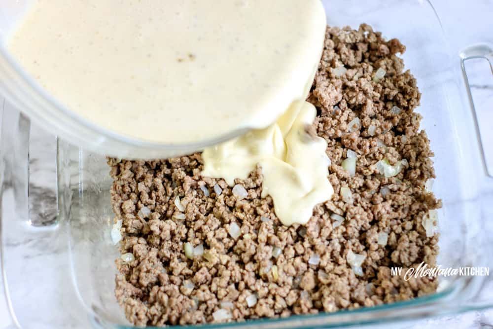 pouring cream mixture over browned burger in casserole dish