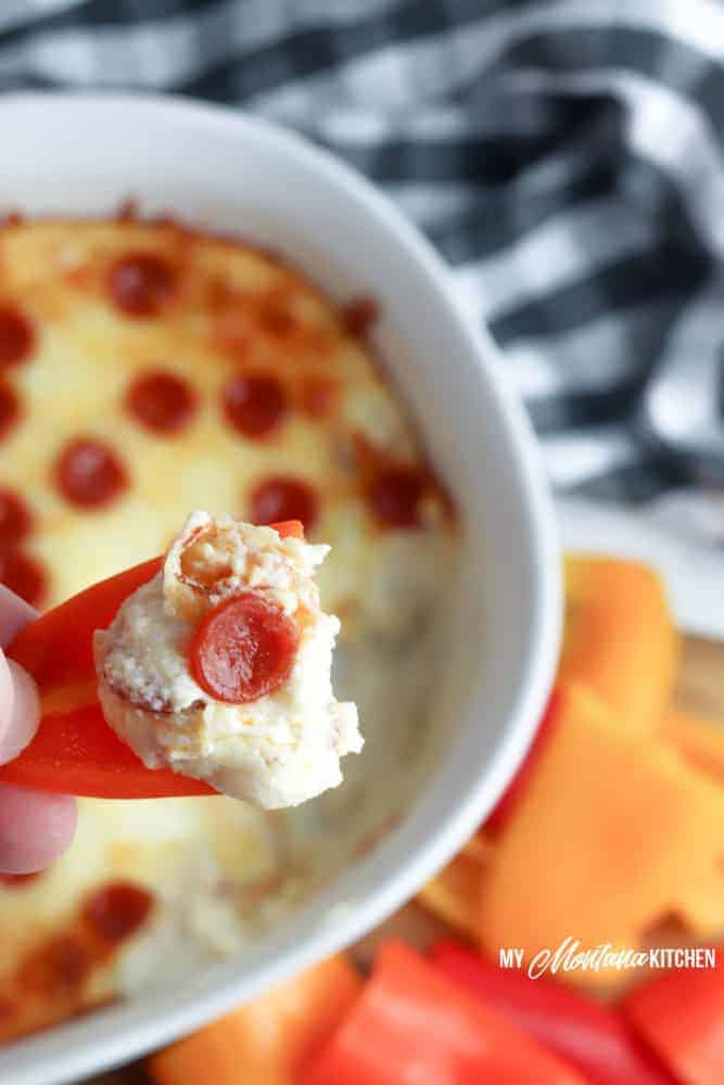 Red peppers being dipped in low carb cheesy pepperoni dip