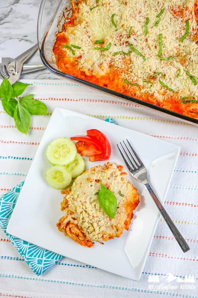 chicken parm casserole on white plate with cucumbers and tomatoes