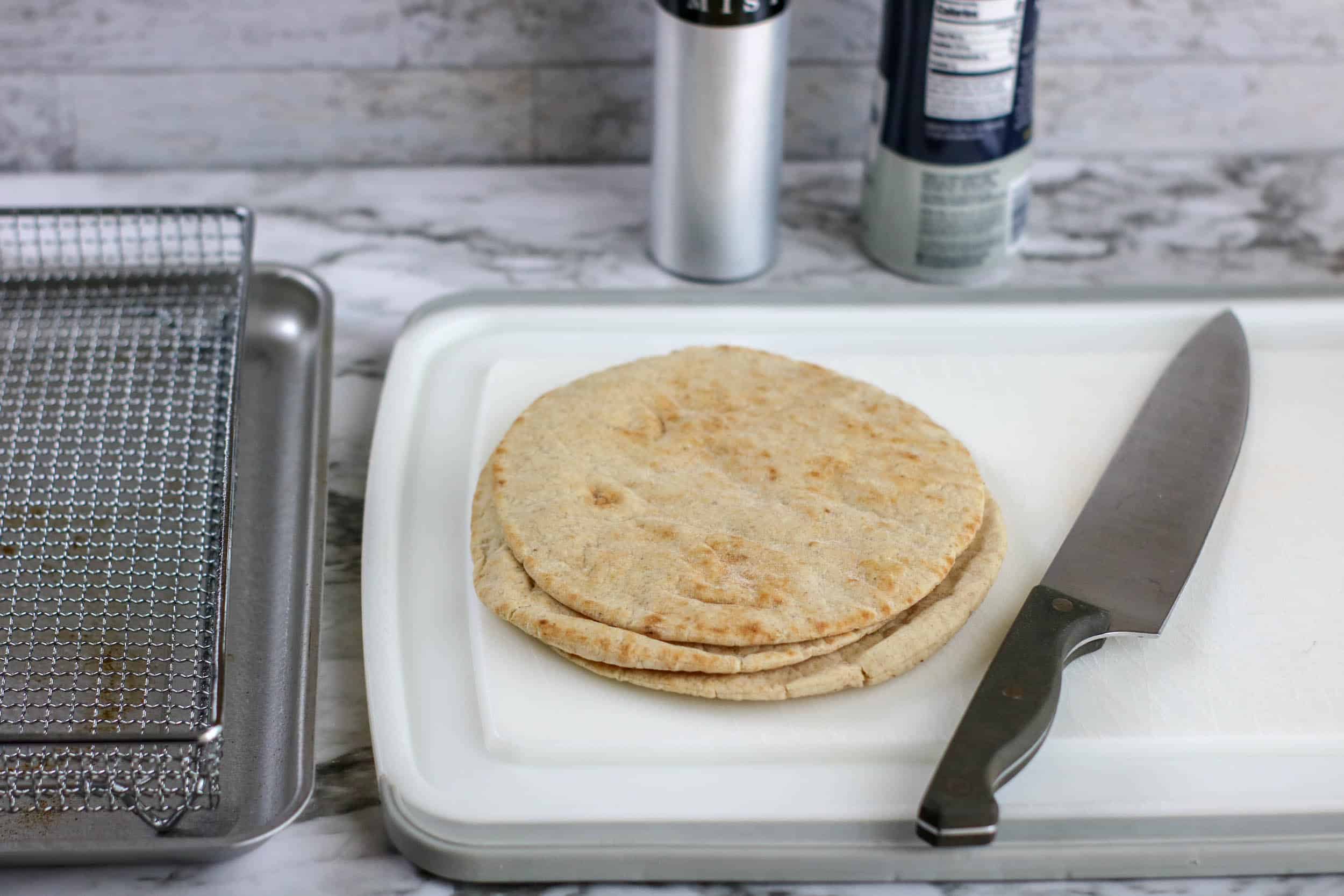 uncut pita bread with knife on white cutting board