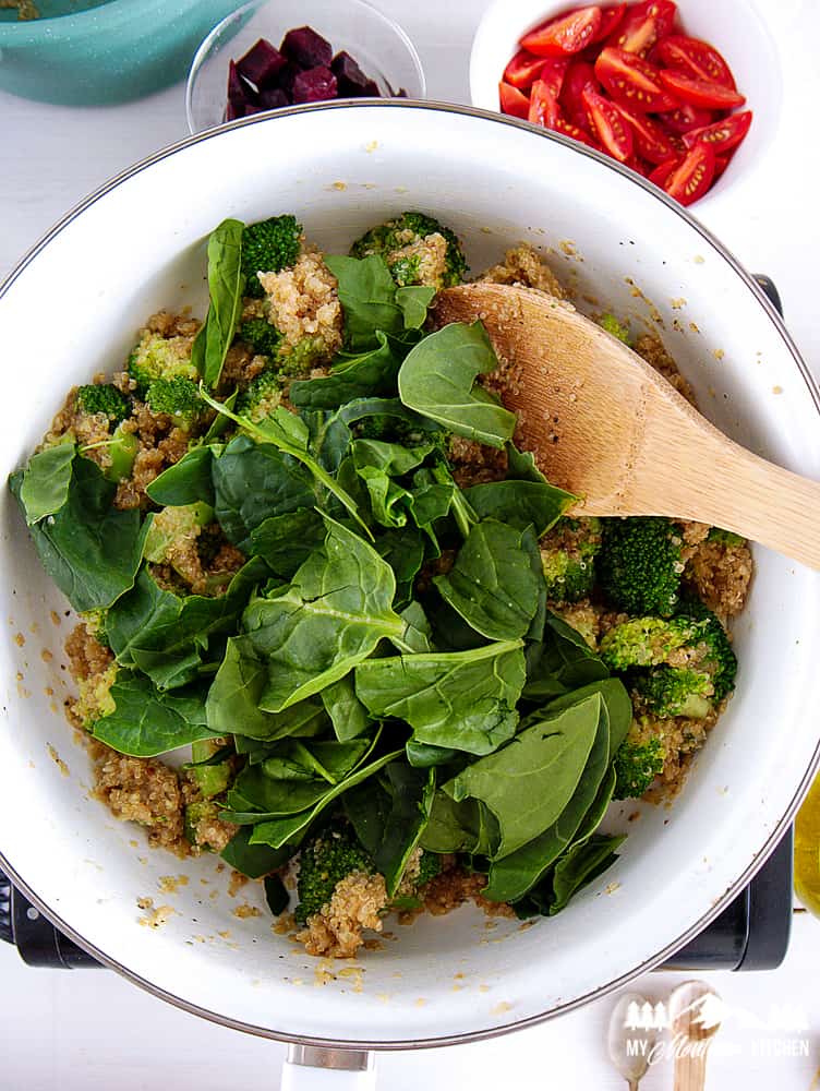 adding spinach to cooked broccoli and quinoa