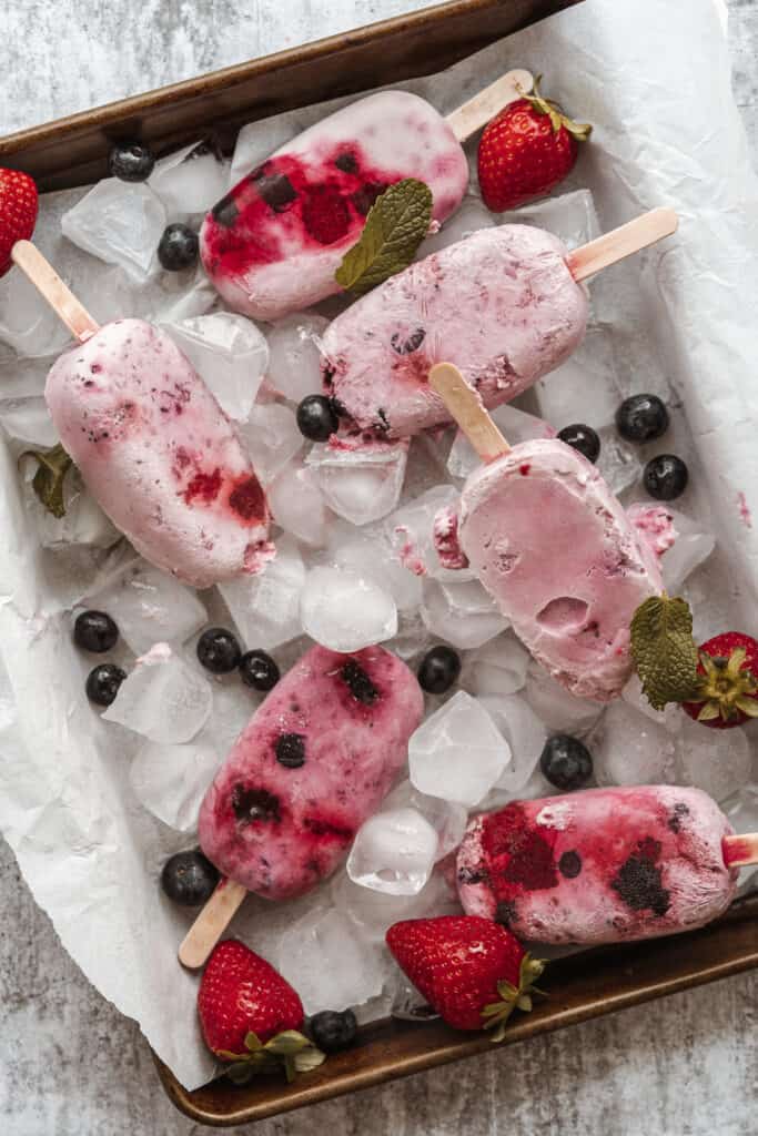 mixed berry popsicles on parchment lined baking sheet with fruit and ice