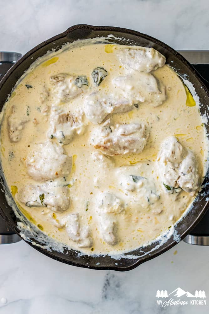 cooked chicken thighs in iron skillet with basil cream sauce
