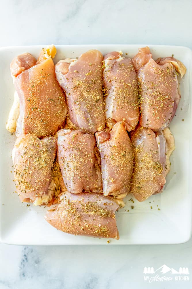 raw chicken thighs with seasoning on white plate