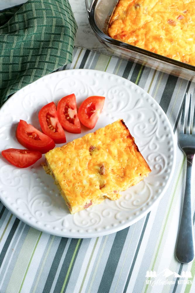ham egg and cheese casserole on white plate with wedges of tomatoes
