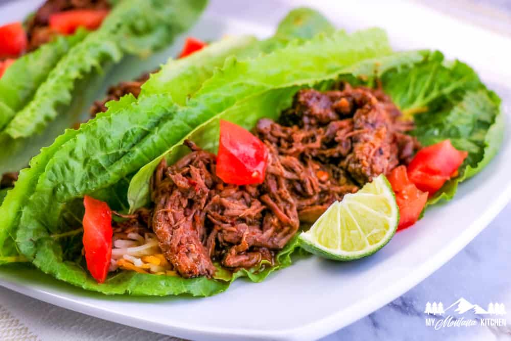 close up of barbacoa beef in lettuce wrap with tomatoes and lime wedge