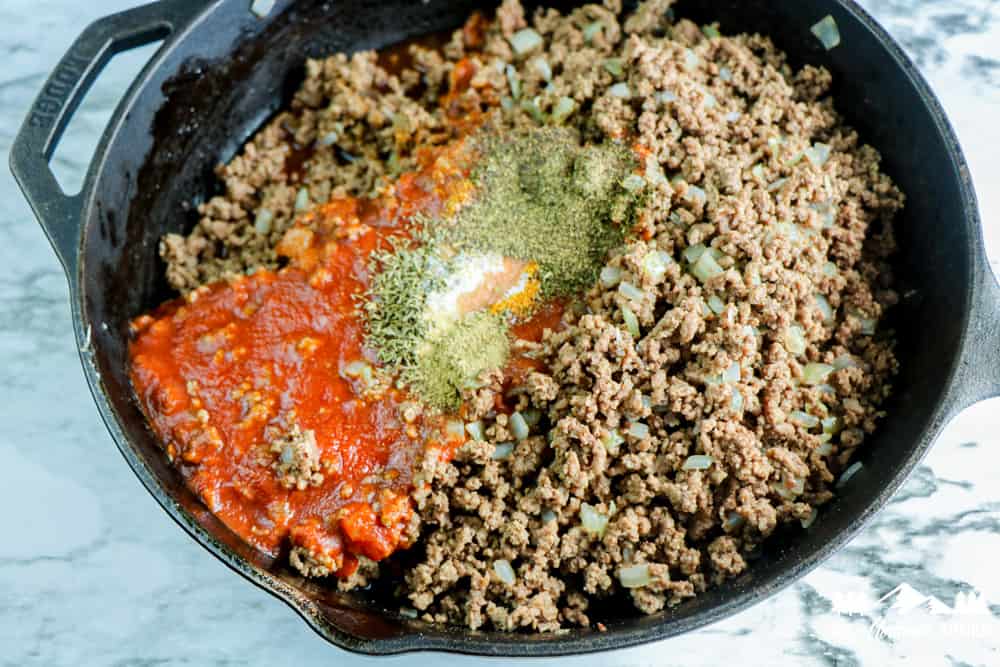 browned burger in skillet with tomato sauce and spices