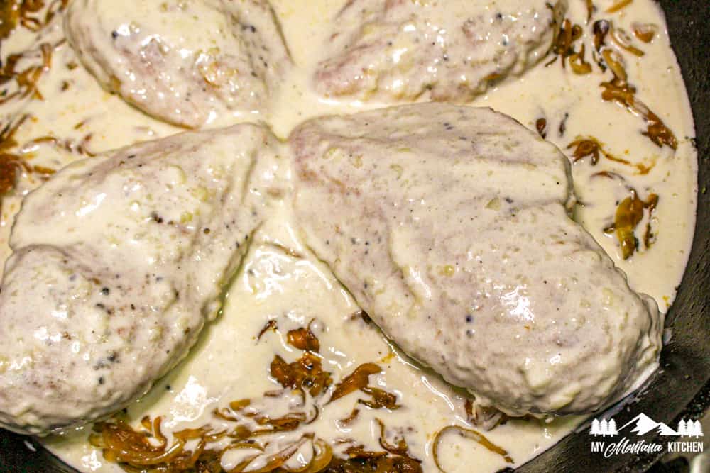 creamy sauce over chicken and onions in skillet