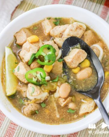 green chile chicken soup in white bowl with dark spoon