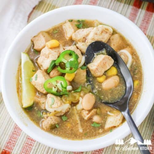 green chile chicken soup in white bowl with dark spoon