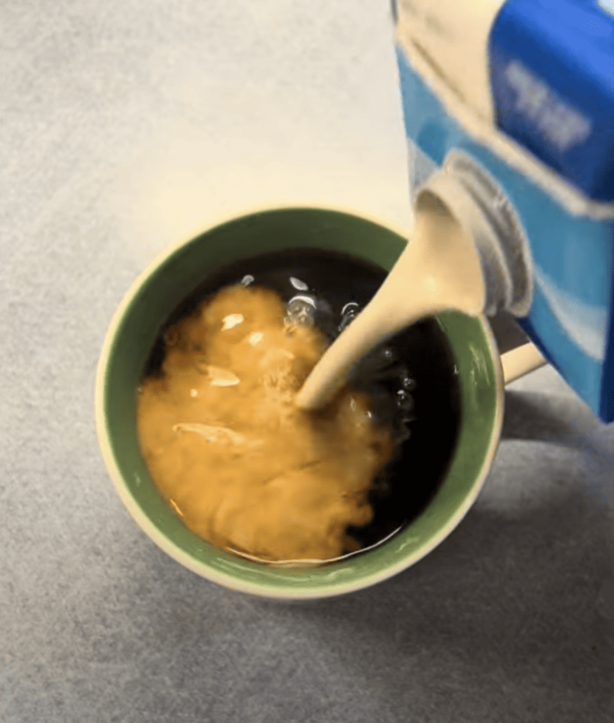 container pouring half and half into coffee
