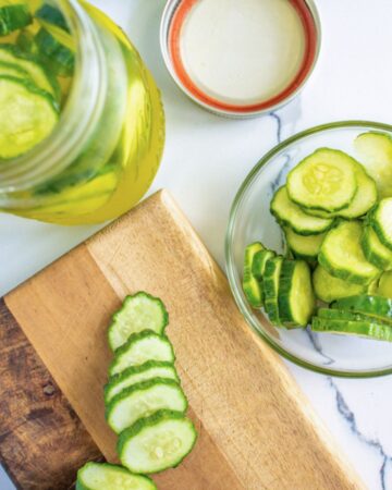 sliced cucumbers on cutting board and pickles in mason jar