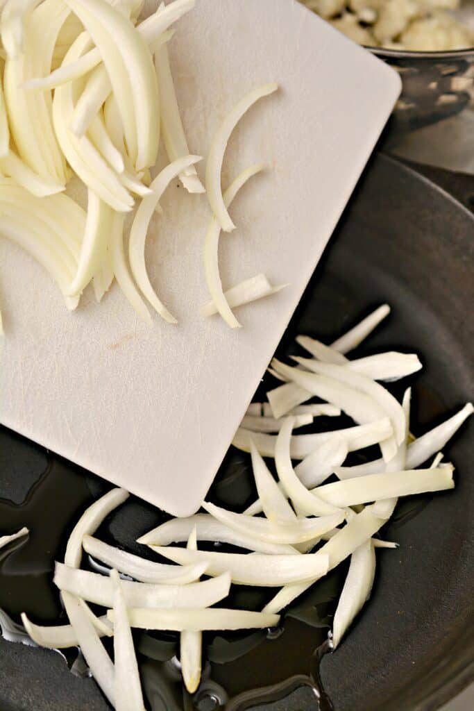 sliced onions on white cutting board and in iron skillet