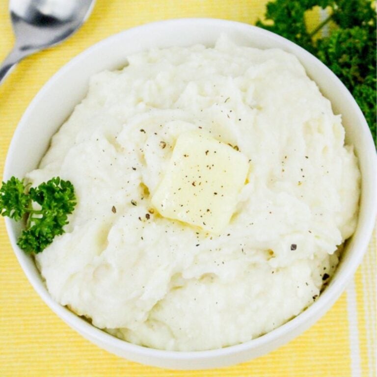 Bowl of cottage cheese mashed potatoes topped with a pat of butter and freshly ground pepper, on a yellow background.