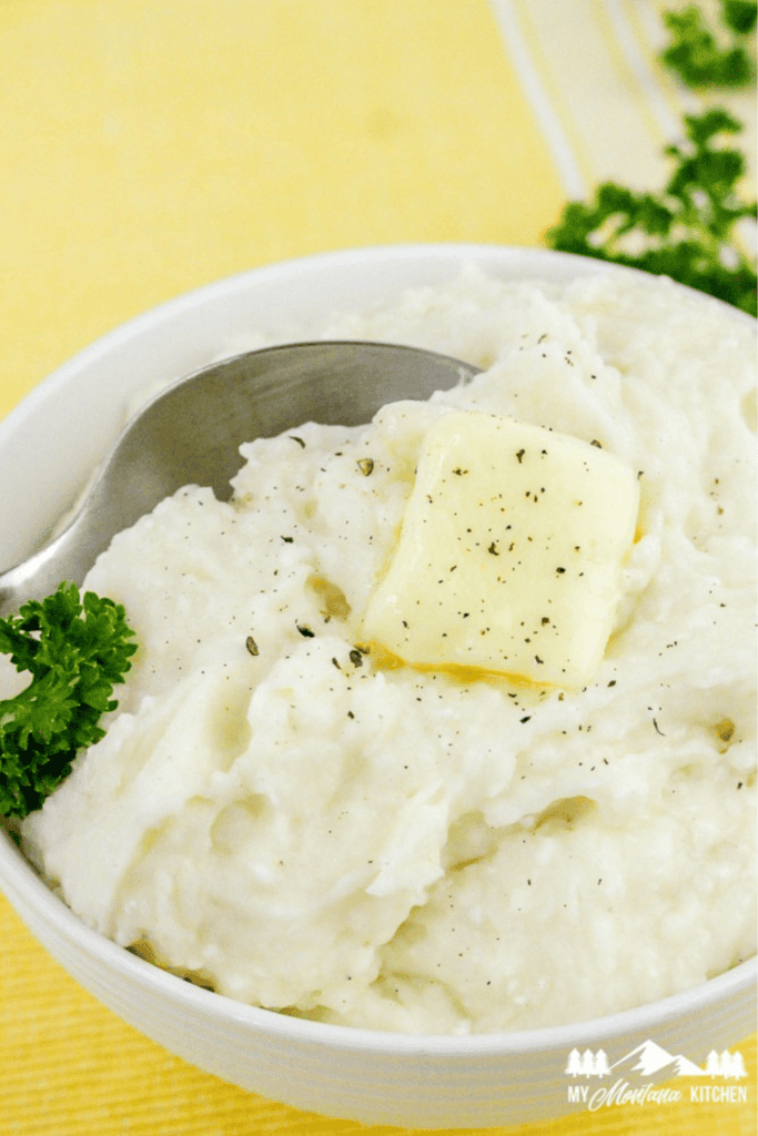 Creamy mashed potatoes served in a white bowl, topped with melted butter and pepper, garnished with parsley.