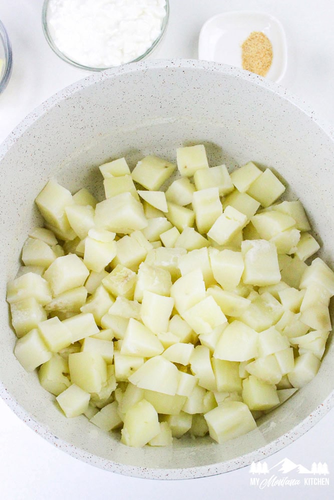 Cooked, drained potatoes in a pot, ready to be mashed with added ingredients like cottage cheese and seasonings.