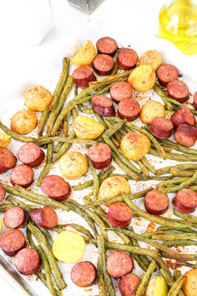Overhead shot of a fully roasted smoked sausage, potato, and green bean meal on a baking sheet, ready to serve.