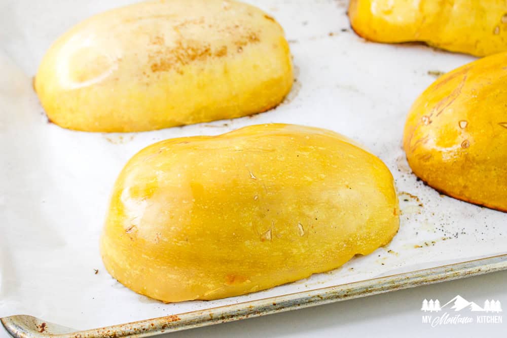 Whole spaghetti squash halves roasted upside down on a baking tray with golden skin.