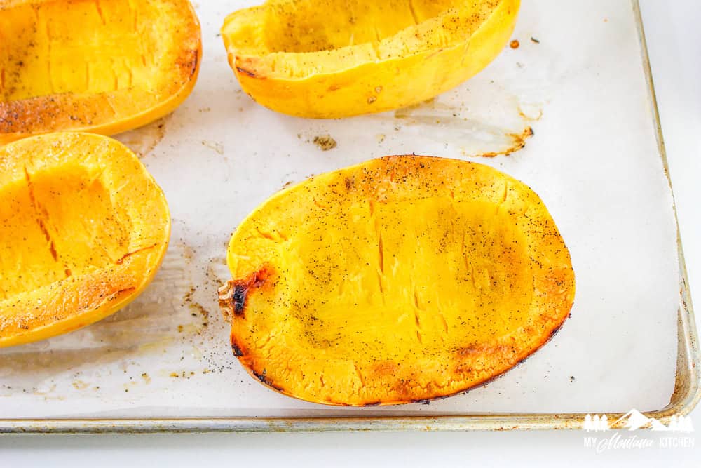 Baking sheet with roasted spaghetti squash halves seasoned with salt and pepper.