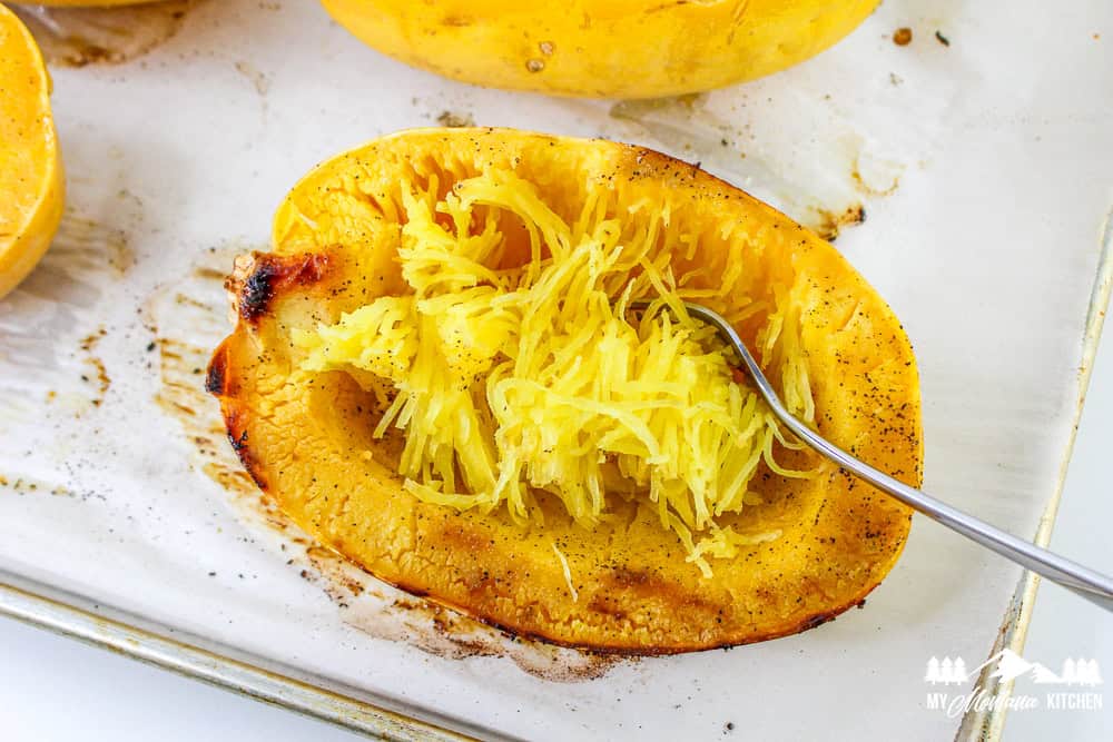 Roasted spaghetti squash half being scraped with a fork to create noodle-like strands.