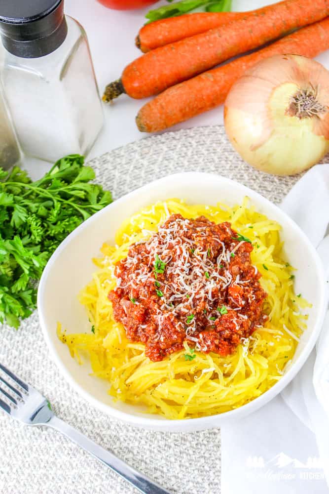 Top view of roasted spaghetti squash topped with meat sauce and grated cheese, served with a silver fork.