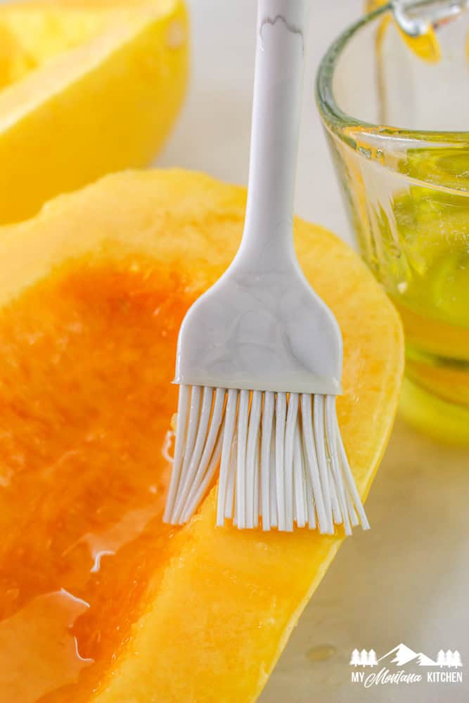 Close-up of a pastry brush applying oil to the inside of a halved spaghetti squash.