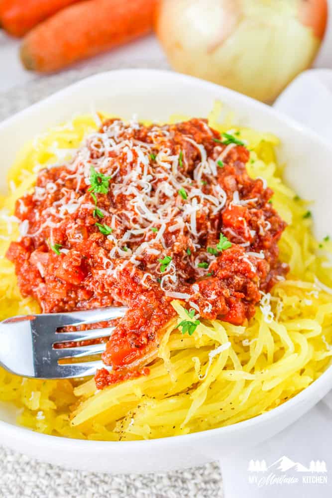 Close-up of spaghetti squash topped with hearty Bolognese sauce, sprinkled with shredded Parmesan and garnished with fresh parsley.