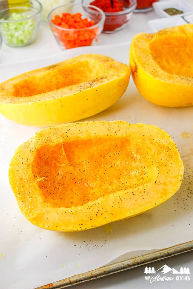 Halved spaghetti squash on a baking sheet, seasoned with salt and pepper, ready for roasting.