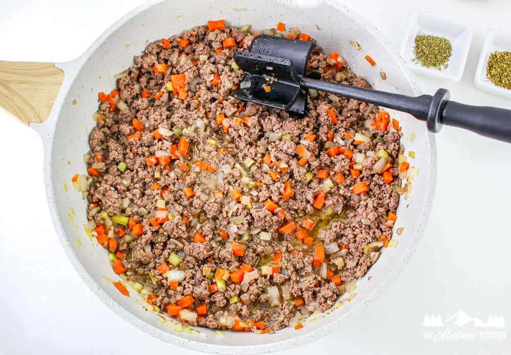 Ground beef sautéing with diced carrots, onions, and celery in a large skillet.