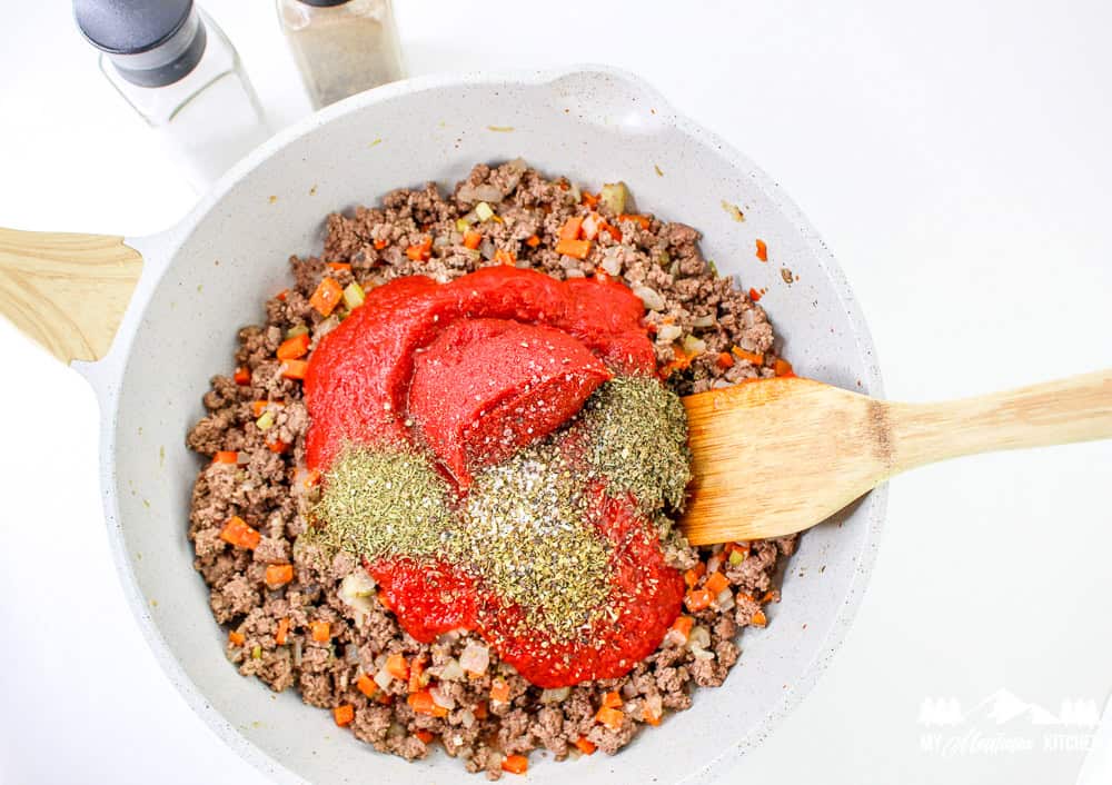 Ground beef, tomato paste, Italian herbs, and veggies in a skillet ready to be mixed into a Bolognese sauce.