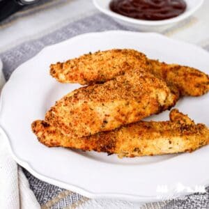 Close-up of crispy parmesan crusted chicken tenders on a white plate with sauce