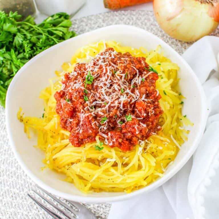 Bowl of roasted spaghetti squash topped with a hearty Bolognese meat sauce, garnished with grated Parmesan and fresh parsley.