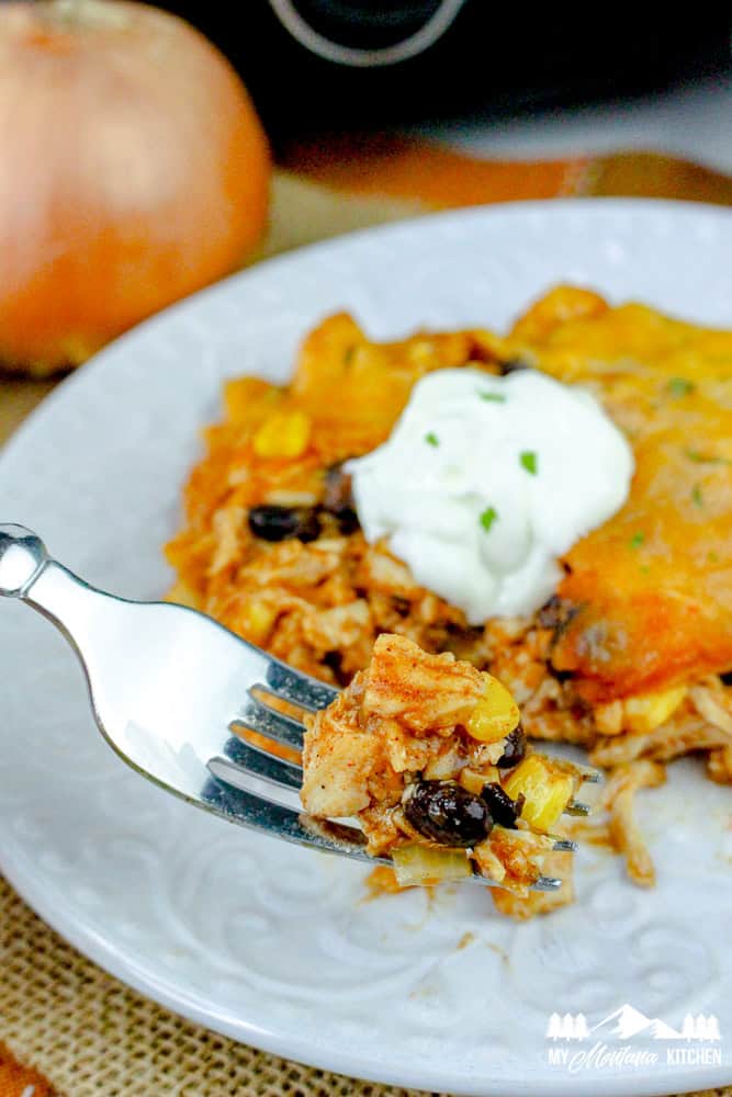 Fork holding a bite of chicken enchilada casserole with corn, beans, and cheese.
