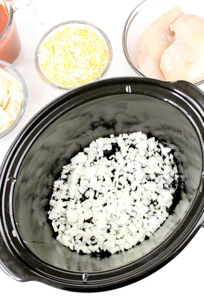 Diced white onions in the bottom of a slow cooker to start enchilada casserole recipe.