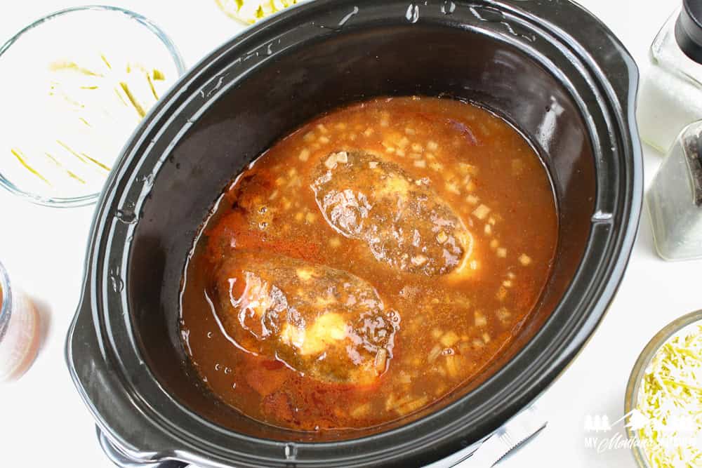Chicken breasts cooking in enchilada sauce in a slow cooker.