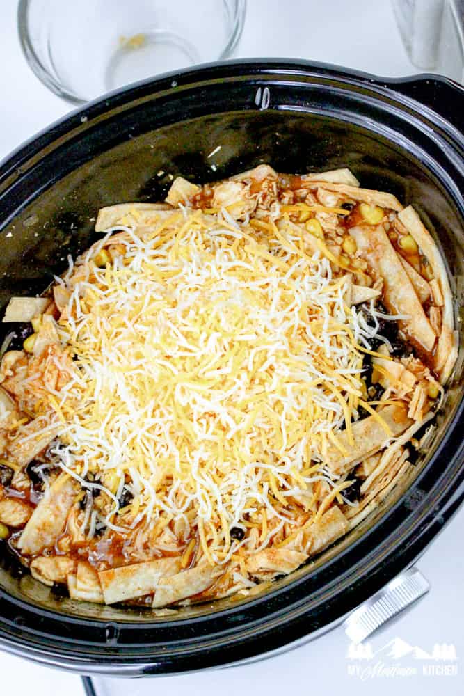 Crockpot enchilada casserole with shredded cheese layered over tortillas, beans, and sauce.