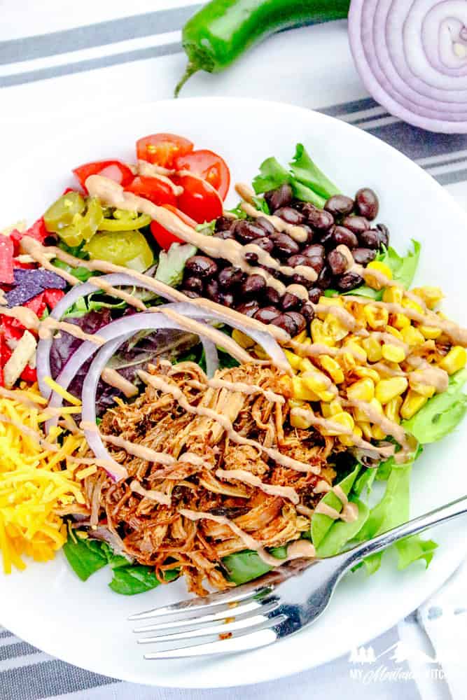Assembled pulled pork salad with greens, corn, black beans, shredded cheese, red onion, tomatoes, jalapeños, and BBQ ranch dressing.