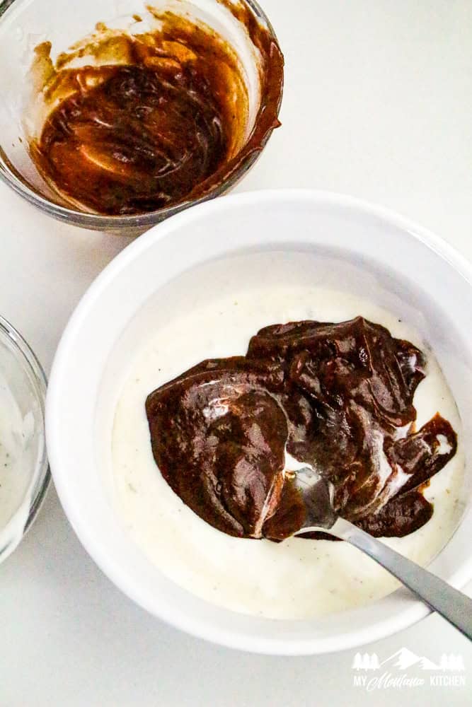 Mixing BBQ sauce with ranch dressing in a white bowl to make salad dressing.
