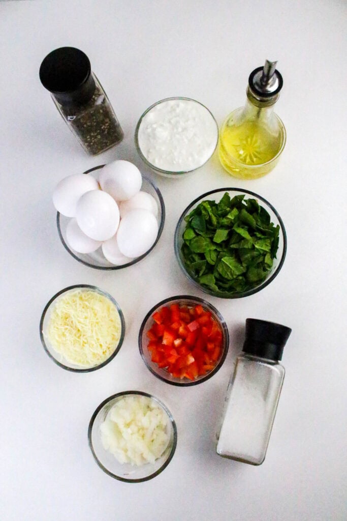 Overhead view of all ingredients for a cottage cheese frittata laid out in glass bowls