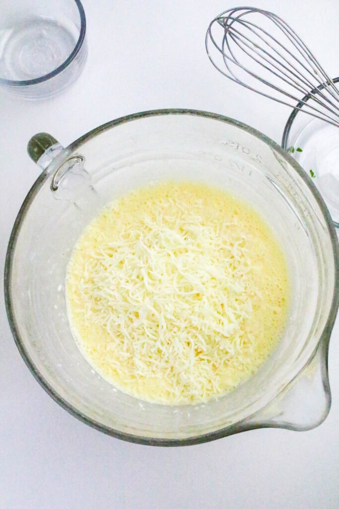 Shredded mozzarella cheese in a mixing bowl with whisked eggs and cottage cheese