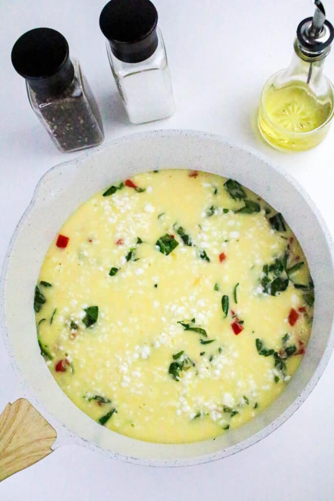 Uncooked egg and cottage cheese mixture with spinach and red bell pepper in a skillet, ready to bake