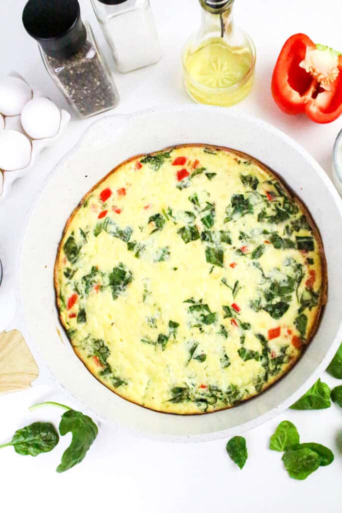 Fully baked cottage cheese frittata in a white oven-safe skillet, surrounded by eggs, bell pepper, oil, and seasonings