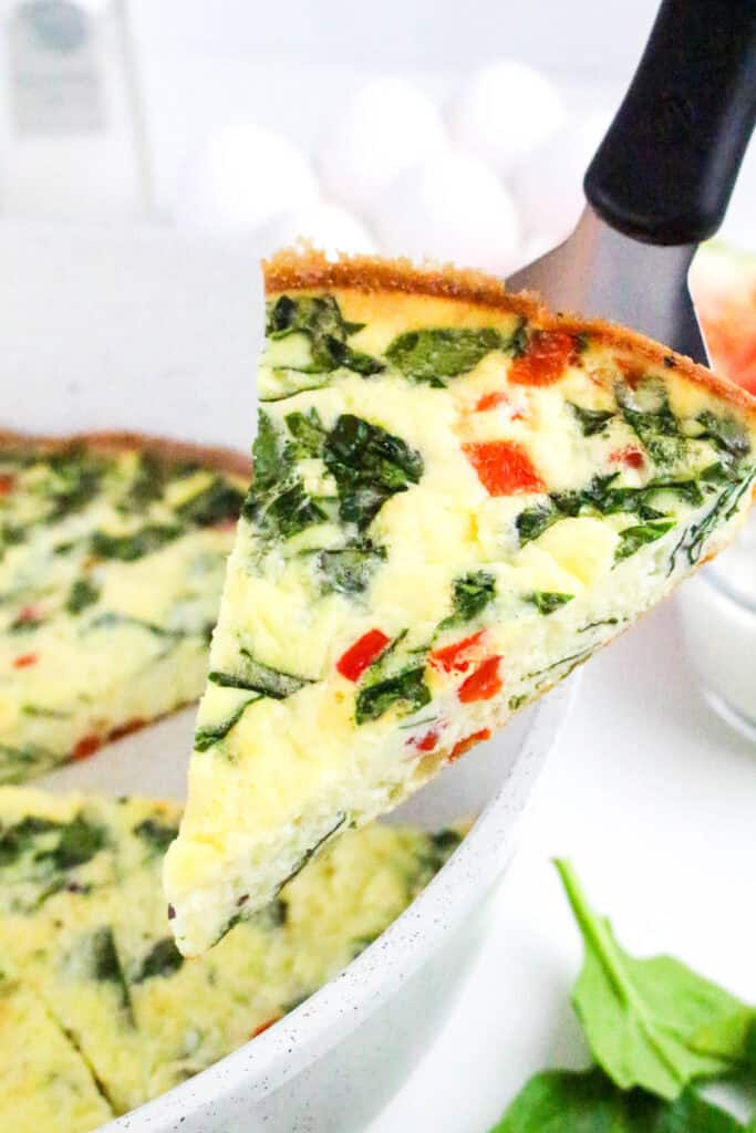 Slice of cottage cheese frittata with spinach and red bell pepper being served from a skillet