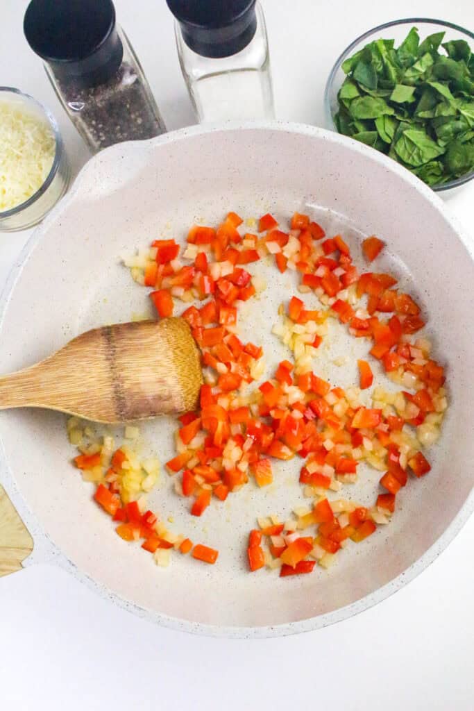 Chopped onion and red bell pepper being sautéed in a white non-stick skillet