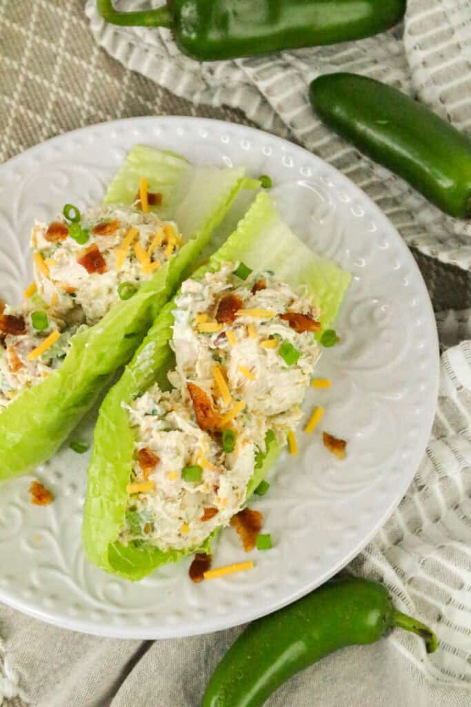 Overhead view of jalapeño popper chicken salad lettuce wraps on a white plate, surrounded by fresh jalapeños.