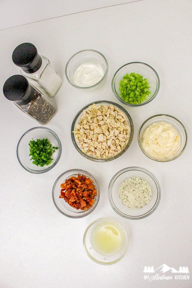 Overhead view of all bacon ranch chicken salad ingredients in small bowls, including chicken, bacon, celery, and dressing.