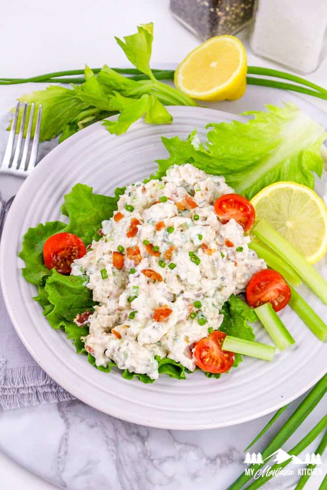 Bright plate of bacon ranch chicken salad on lettuce, surrounded by fresh celery, lemons, and tomatoes.